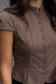 Blusa corta de fit ajustado, manga corta abullonada, cuello mao, peplum con olanes en bajo, cierre frontal con hilera de botones forrados.