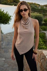 Blusa asimétrica de fit fluido, sin mangas, cuello halter fluido con plisados, escote en espalda y lazo amarrable posterior. Cierre posterior con botón y ojal. Detalle de bajo frontal asimétrico.