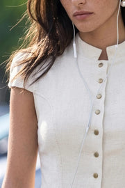 Blusa corta de fit ajustado, pinzas frontales, manga corta abullonada con plisados en hombros, cuello mao y cierre frontal con botones en contraste. Detalle de peplum con olanes y bajo curveado frontal.