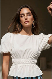 Blusa de manga corta abullonada con plisados en hombros, cuello redondo, rib elástico en cintura y peplum con olanes en bajo. Cierre posterior con botón y ojal.