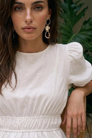 Blusa de manga corta abullonada con plisados en hombros, cuello redondo, rib elástico en cintura y peplum con olanes en bajo. Cierre posterior con botón y ojal.