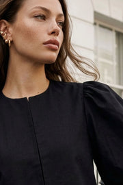 Blusa corta de fit recto, cuello redondo, manga corta amplia globo con volumen en borde, cierre frontal con broches ocultos y bajo curveado frontal.