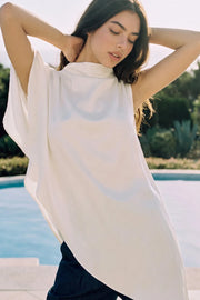 Blusa túnica asimétrica de una manga corta seguida con olanes, cuello mock seguido, bajo asimétrico y cierre posterior con botón y ojal.