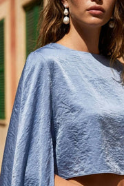 Blusa tipo túnica asimétrica, de cuello redondo, con hombreras, una manga corta seguida, fit fluido y bajo asimétrico.