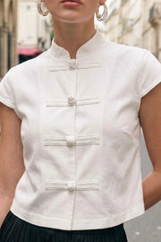 Blusa corta de fit recto, cuello mao, manga corta y cierre frontal con botones alamares.