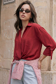 Camisa corta de fit recto, manga larga rolled up con trabilla ajustable, cuello camisero, cruce frontal con escote v y nudo decorativo en bajo. Detalle de bajo curveado y pinza de amplitud en espalda.