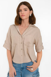 Camisa corta de fit recto, manga corta con doblez en borde y trabillas decorativas laterales, bolsillos frontales de parche, cuello camisero, bajo curveado y pinza de amplitud en espalda. Cierre frontal con hilera de botones en contraste