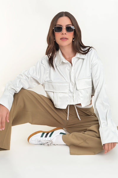 Camisa corta satinada de manga larga con puño abotonado, cuello camisero, fit ligeramente oversized, bolsillos frontales cargo con cartera y cierre frontal con hilera de botones.