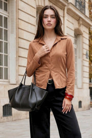 Camisa ajustada de gamuza, pinzas frontales, cuello camisero, bajo curveado, manga larga con amplitud y puño abotonado. Cierre frontal con hilera de botones.