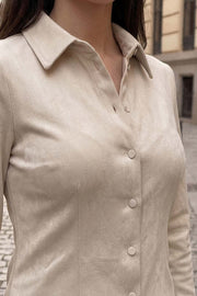 Camisa de gamuza, fit ajustado, cuello camisero, manga larga con puño abotonado, pinzas, bajo curveado y cierre frontal con hilera de botones.
