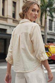 Camisa corta de fit recto, manga larga rolled up con trabilla ajustable, cuello camisero, cruce frontal con escote v y nudo decorativo en bajo. Detalle de bajo curveado y pinza de amplitud en espalda.
