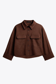 Camisa corta de fit oversized, manga 3/4 amplia con doblez en puños, cuello camisero, bolsillos frontales decorativos con cartera y pinza de amplitud en espalda. Cierre frontal con hilera de botones.