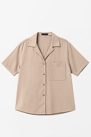 Camisa corta de lino, fit recto, manga corta, cuello camisero, bolsillo frontal de parche, bajo curveado con aberturas laterales y cierre frontal con hilera de botones.