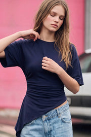 Camiseta de fit fluido, manga corta, cuello redondo, plisados en costados y bajo asimétrico con detalle decorativo lateral.