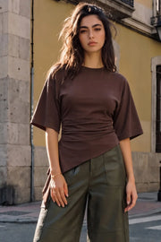 Camiseta de fit fluido, manga corta, cuello redondo, plisados en costados y bajo asimétrico con detalle decorativo lateral.