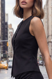 Chaleco ajustado con pinzas, cuello redondo, bajo v frontal con abertura y cierre con hilera de botones. Detalle de trabilla con hebilla posterior en contraste.