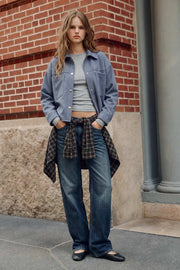 Chamarra corta de gamuza, fit oversized, cuello camisero, manga larga con puño abotonado, corte de bata frontal y posterior, bolsillos frontales de parche y cierre frontal con hilera de botones en contraste.