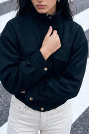 Chamarra de fit oversized, manga larga con puño abotonado, cuello alto, bolsillos delanteros de parche con cartera, cortes decorativos y pretina elástica. Cierre frontal con cremallera oculta y botones en contraste. Detalle de rib elástico en bajo.