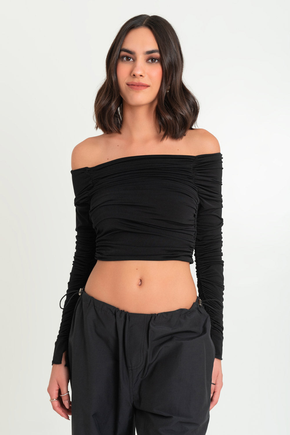 Crop top de fit ajustado, plisados en costados, hombros desubiertos, escote recto con plisados y manga larga plisada con abertura en puño. 