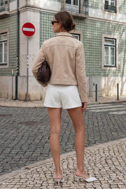 Falda short corto de fit ajustado, cintura alta, cruce frontal con bajo curveado y vivos decorativos posteriores. Cierre lateral con cremallera oculta.