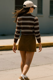 Falda short corto de gamuza, corte en a, cintura alta con pretina, abertura frontal en bajo y cierre lateral con cremallera oculta. Detalle de cinturón decorativo con hebilla en contraste.