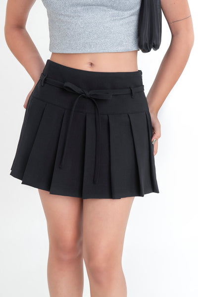 Falda short corto tableado, de corte en a, cintura alta con pretina, trabillas y lazo amarrable del tejido. Detalle de tableado en bajo y cierre lateral con cremallera oculta.