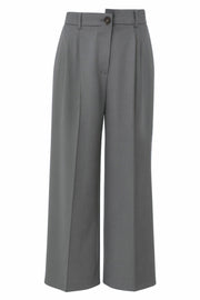 Pantalón de fit wide leg, pinzas frontales, cintura media, pretina con detalle asimétrico y trabillas, bolsillos delanteros y detalle de raya. Cierre frontal con botón y cremallera oculta.