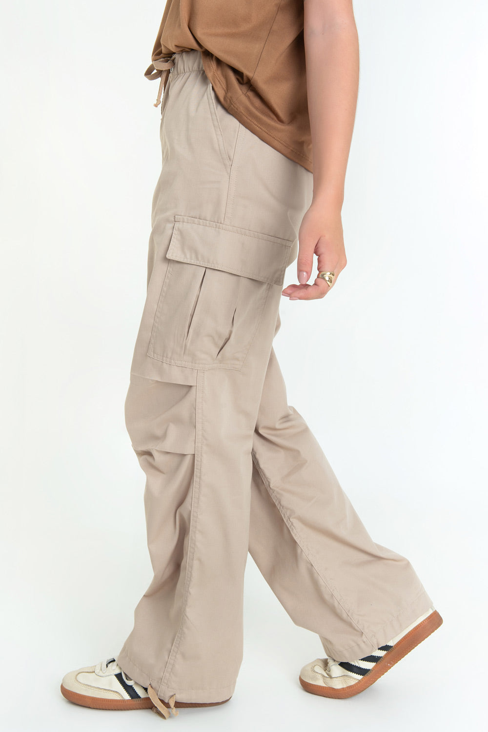 Pantalón cargo de cintura alta elástica con jareta frontal ajustable, fit amplio, plisados decorativos en rodillas, bolsillos delanteros, laterales cargo con cartera y traseros de parche. Detalle de bajo con jaretas ajustables, cierre frontal con botón y cremallera oculta.