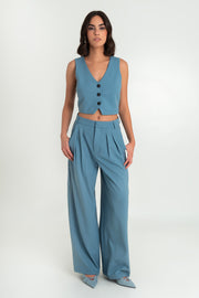 Pantalón de fit wide leg, cintura alta con pretina y trabillas, bolsillos delanteros y pinzas frontales. Cierre frontal con broche y cremallera oculta.