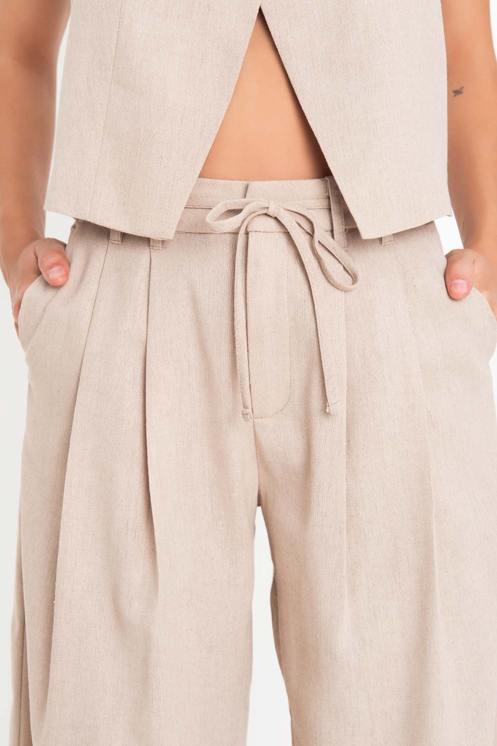 Pantalón de lino, fit wide leg, cintura alta con pretina, trabillas y jareta frontal ajustable. Detalle de pinzas frontales, bolsillos delanteros y vivo decorativo posterior. Cierre frontal con broche y cremallera ocultos.