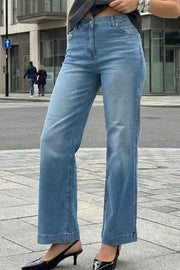 Pantalón de denim, fit recto, cintura alta con pretina y trabillas, bolsillos delanteros y traseros de parche. Cierre con botón y cremallera oculta.