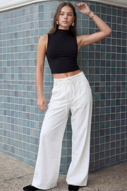 Pantalón de fit wide leg, cintura alta con pretina, trabillas y doble lazo amarrable, pinzas frontales y bolsillos delanteros. Cierre frontal con broche y cremallera ocultos.