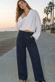 Pantalón de fit wide leg, cintura alta con pretina, trabillas y doble lazo amarrable, pinzas frontales y bolsillos delanteros. Cierre frontal con broche y cremallera ocultos.