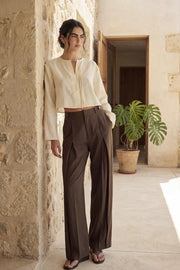 Pantalón de fit wide leg, cintura alta con pretina y trabillas, pinzas frontales, bolsillos delanteros, vivos decorativos posteriores, cierre frontal con broche y cremallera ocultos. Detalle de trabillas laterales ajustables en cintura.