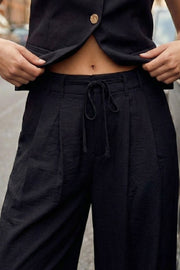Pantalón de fit recto, pinzas frontales, cintura alta con pretina y trabillas, bolsillos delanteros, vivo decorativo posterior, cierre frontal con broche y cremallera ocultos. Detalle de jareta frontal ajustable en cintura.