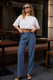 Pantalón de fit wide leg, cintura alta con pretina y trabillas, pinzas frontales con raya frontal, bolsillos delanteros, vivo decorativo posterior, cierre frontal con broche y cremallera ocultos.