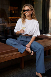 Pantalón de fit wide leg, cintura alta con pretina y trabillas, pinzas frontales con raya frontal, bolsillos delanteros, vivo decorativo posterior, cierre frontal con broche y cremallera ocultos.
