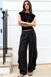 Pantalón fluido de fit wide leg, cintura alta con pretina, pinzas frontales con detalle decorativo, bajo curveado asimétrico con olanes y detalle de abertura laterales. Cierre lateral con cremallera oculta.