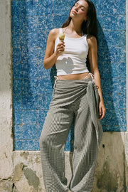 Pantalón fluido de fit palazzo, estampado cuadros, cintura media con pretina elástica, plisados en costado y detalle de pareo decorativo con nudo lateral.