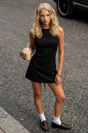 Playsuit de fit ajustado, cuello barco, sin mangas, pinzas frontales, lazo amarrable posterior y cierre con cremallera oculta.