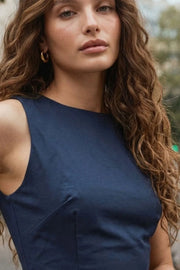 Playsuit de fit ajustado, cuello barco, sin mangas, pinzas frontales, lazo amarrable posterior y cierre con cremallera oculta.