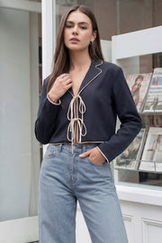 Top blazer corto de fit fluido, manga larga, escote v con solapa y cierre frontal con lazos amarrables. Detalle de ribete decorativo en contraste.
