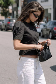 Blusa corta de fit recto, manga corta globo con plisados en hombro, cortes frontales con pinzas, cuello redondo y cierre frontal con hilera de botones.
