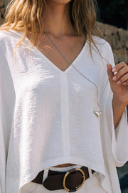 Blusa tipo capa de fit fluido, manga larga amplia, cuello v y bajo asimétrico. Detalle de textura en tejido.