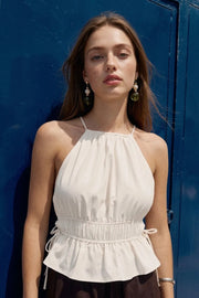 Top corto de cuello halter con plisados, tirantes delgados, detalle de rib con plisados y lazos laterales en costados, peplum con olanes en bajo y cierre posterior con botón y ojal.