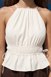 Top corto de cuello halter con plisados, tirantes delgados, detalle de rib con plisados y lazos laterales en costados, peplum con olanes en bajo y cierre posterior con botón y ojal.