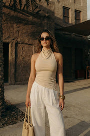 Top halter corto de fit ajustado, sin mangas, cuello halter fluido con plisados y escote en espalda. Detalle de bajo diagonal asimétrico.