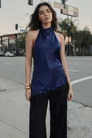 Blusa halter satinada de fit fluido, cuello halter fluido, sin mangas, bajo asimétrico con abertura lateral y encaje decorativo en contraste. Detalle de escote fluido en espalda, cierre posterior con botón y ojal.