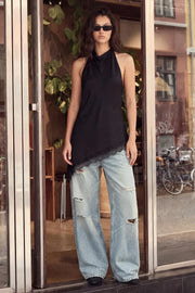 Blusa larga de fit fluido, sin mangas, cuello halter fluido, escote en espalda, bajo asimétrico con encaje en borde y aberturas laterales. Cierre posterior con botón y ojal.