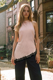 Blusa larga de fit fluido, sin mangas, cuello halter fluido, escote en espalda, bajo asimétrico con encaje en borde y abertura lateral. Cierre posterior con botón y ojal.